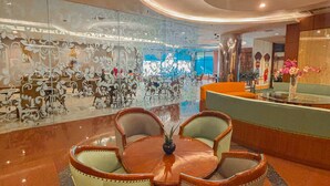 A lobby with a round wooden table surrounded by chairs, a patterned glass wall, and a reception desk. - GiiA Sanno Hotel Pluit Jakarta (Jakarta)