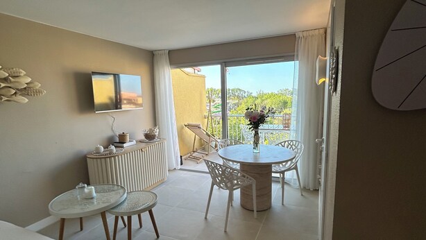 A hotel room with a bed, a small table with chairs, a TV mounted on the wall, and a balcony with a view of the outdoors. - Richelieu vue mer "Soleil, beach 300 m, swimming pool, wifi (Agde)