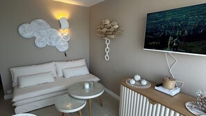 A modern living room with a sofa, two round tables, a TV mounted on the wall, and a decorative wall piece. - Richelieu vue mer "Soleil, beach 300 m, swimming pool, wifi (Agde)