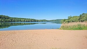 A sandy beach with a calm lake, surrounded by dense greenery and trees.