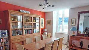A dining area with a wooden table and chairs, a bookshelf, and a window with a view.
