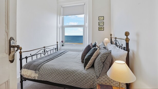 Een slaapkamer met een bed, een bedlamp, een raam met uitzicht op zee en een deur met een deurklink.
