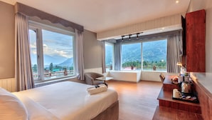 A hotel room with a large bed, a seating area with a table, and a view of mountains through large windows. - Ekaanth by Paradise Chateau (Manali)
