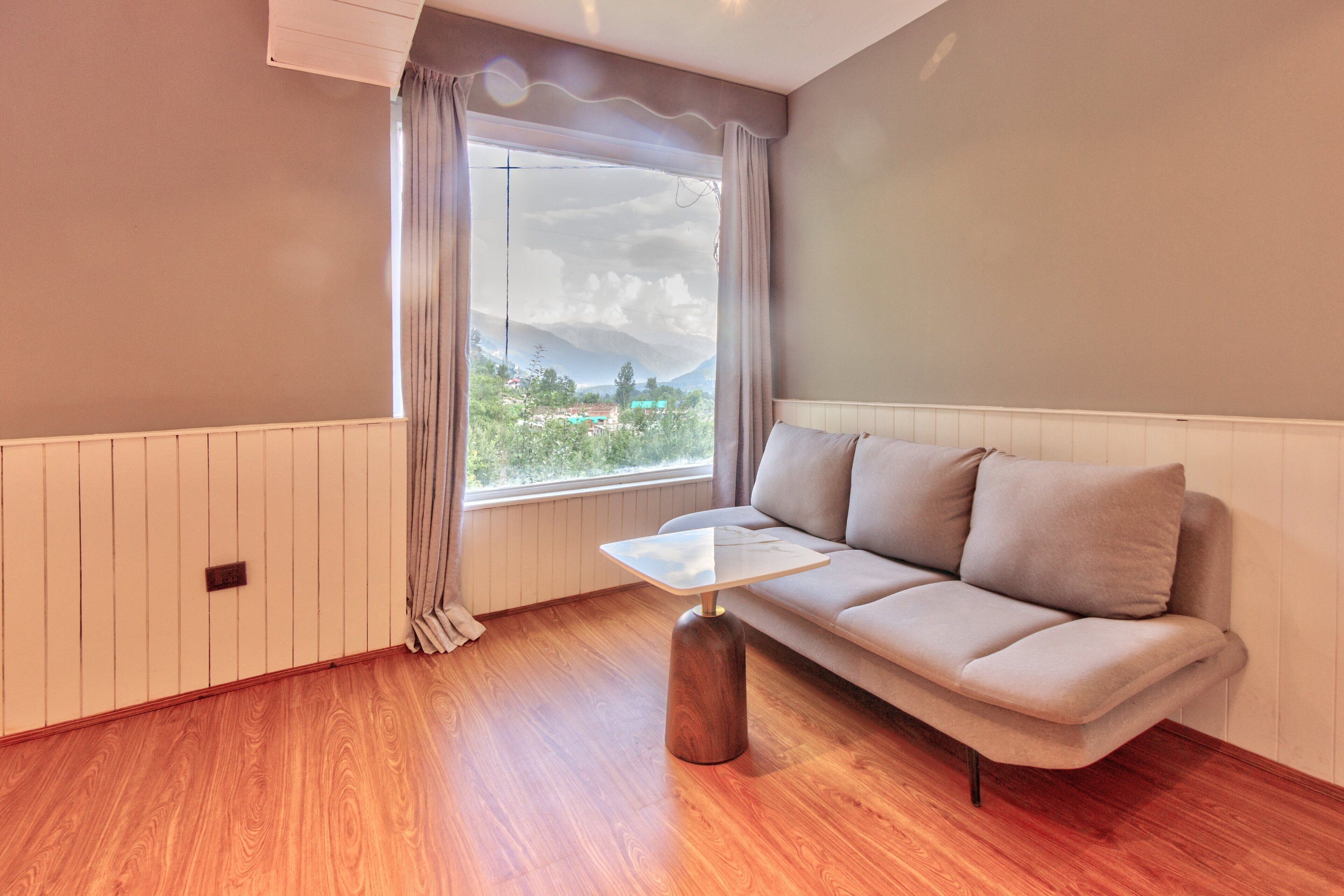 A modern living room with a wooden floor, a beige sofa, a glass coffee table, and a window with curtains.