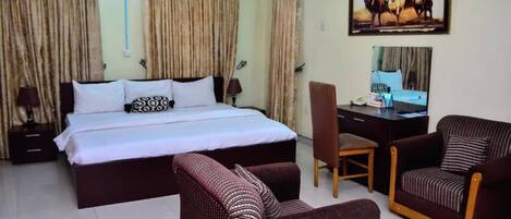 A hotel room with a bed, a desk, two armchairs, a chair, and a painting on the wall.
