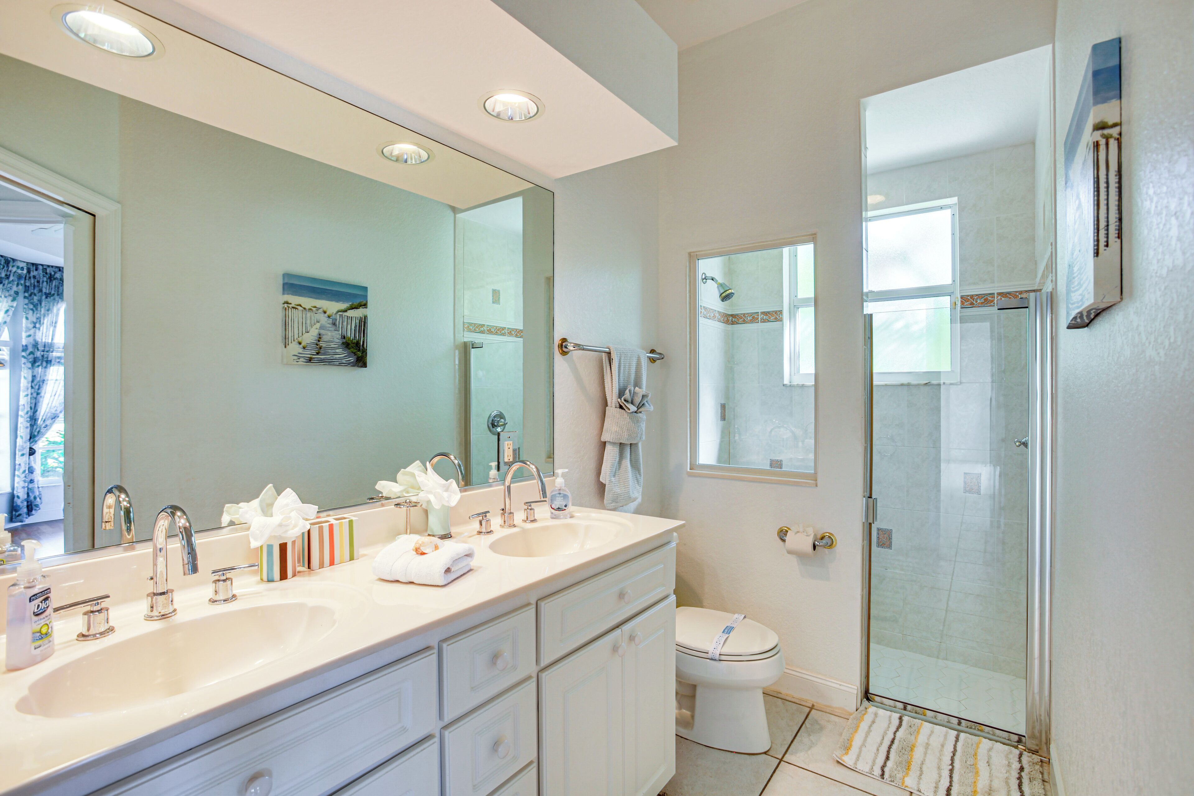 A modern bathroom with dual sinks, a glass shower enclosure, and a large mirror.