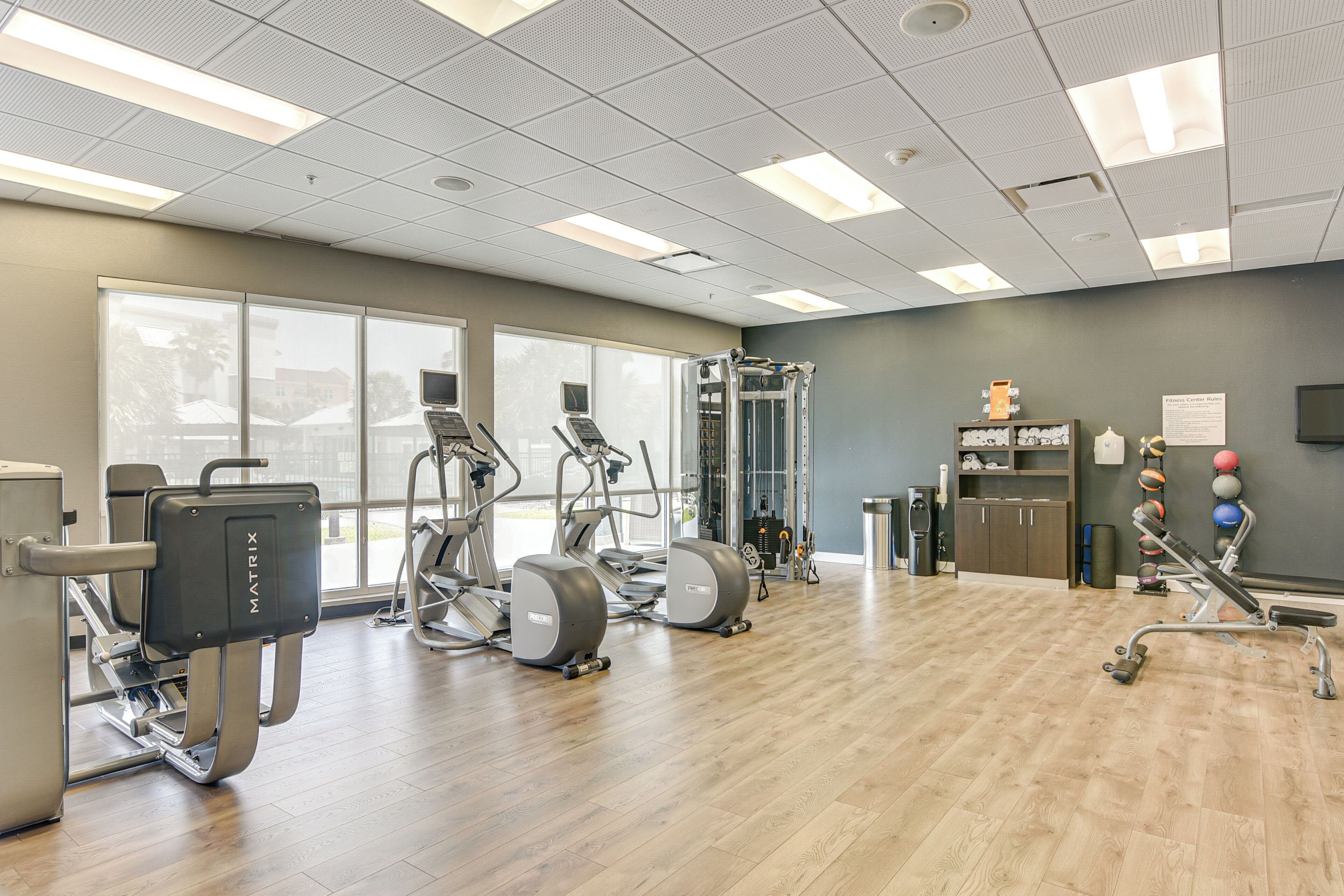 A gym with cardio machines, weightlifting equipment, and a wall-mounted medicine ball rack.
