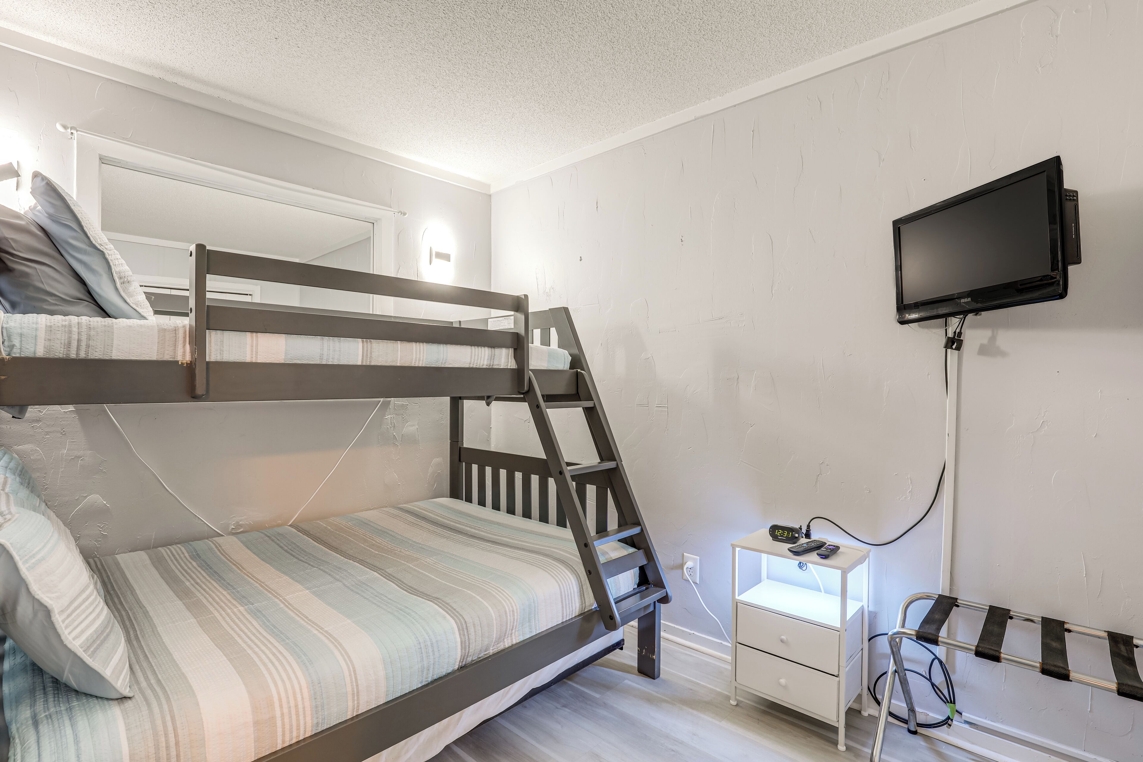 A bunk bed with a TV mounted on the wall, a small desk, and a ladder.