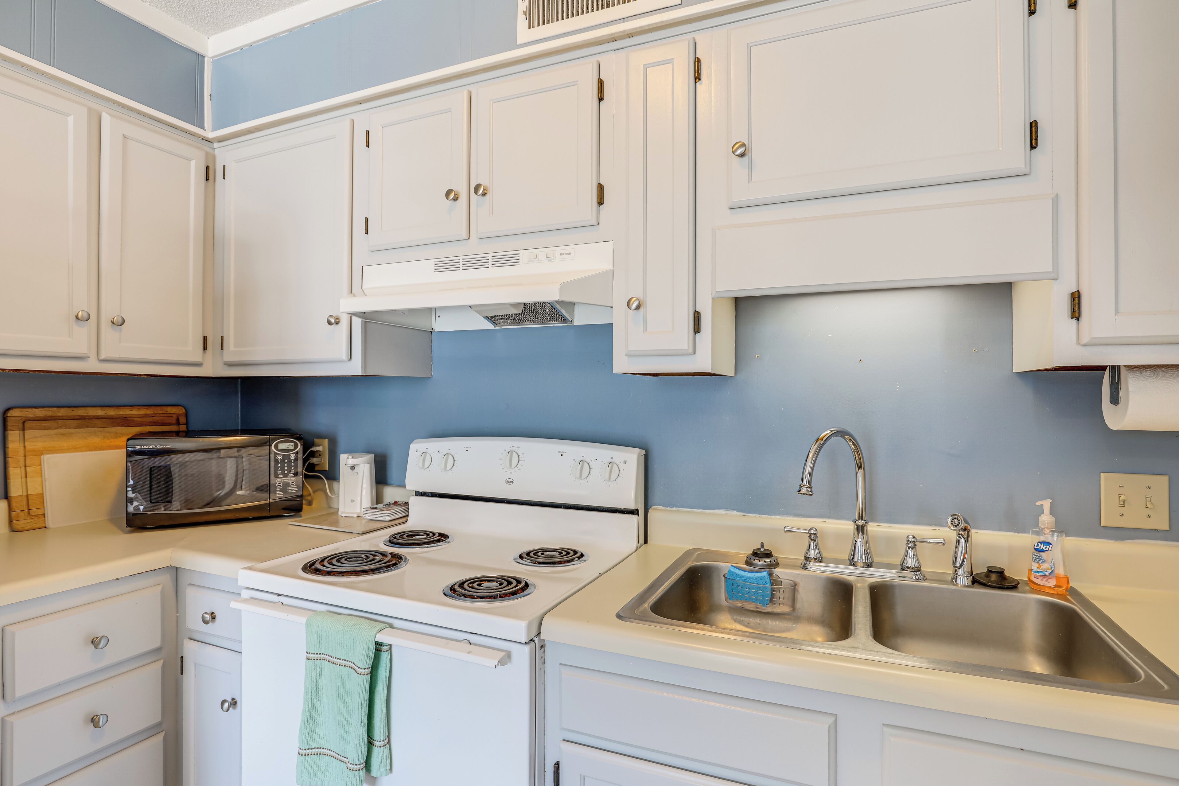 A kitchen with white cabinets, a stove, a microwave, a sink, and a toaster.