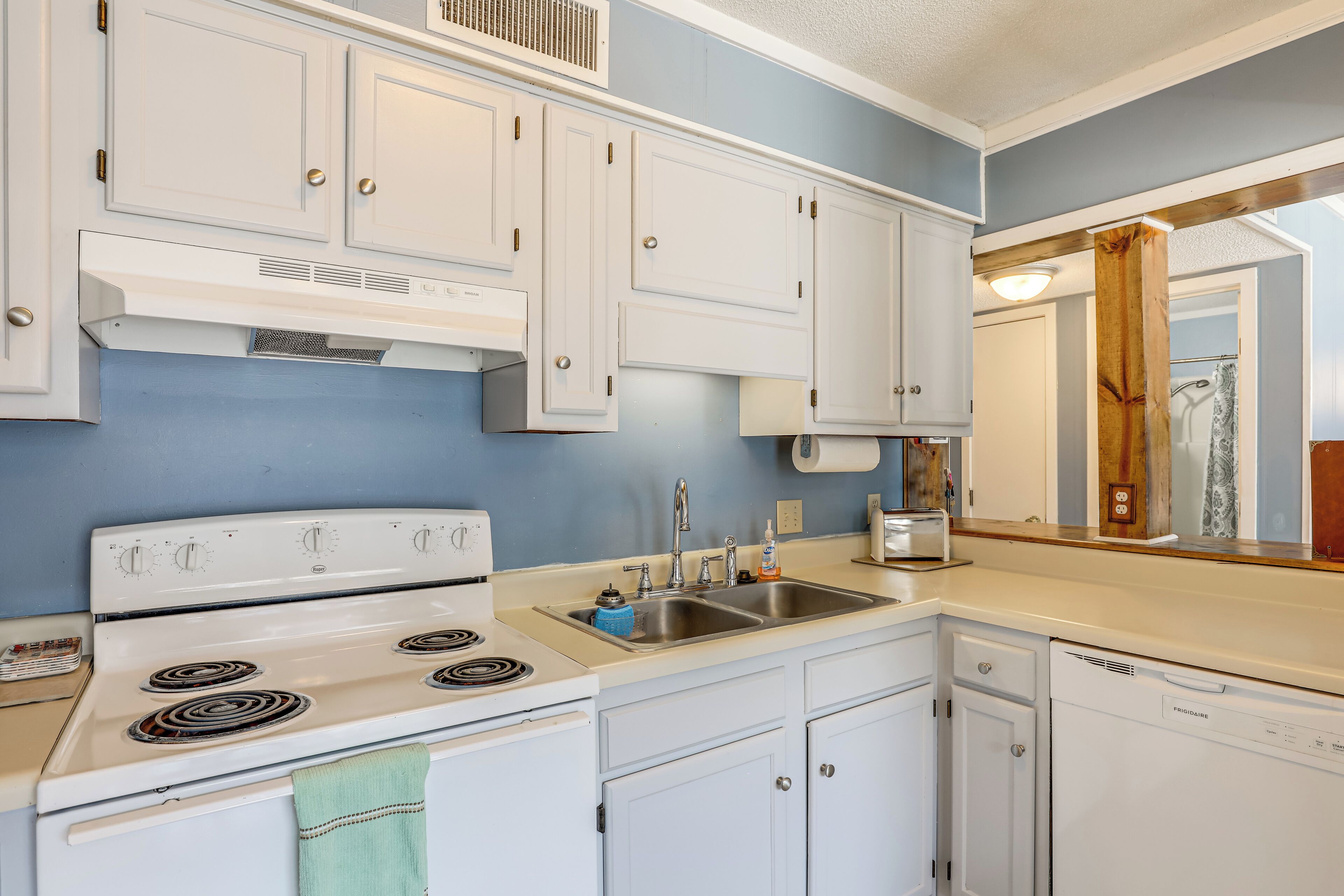 A kitchen with white cabinets, a stove, a sink, and a dishwasher.