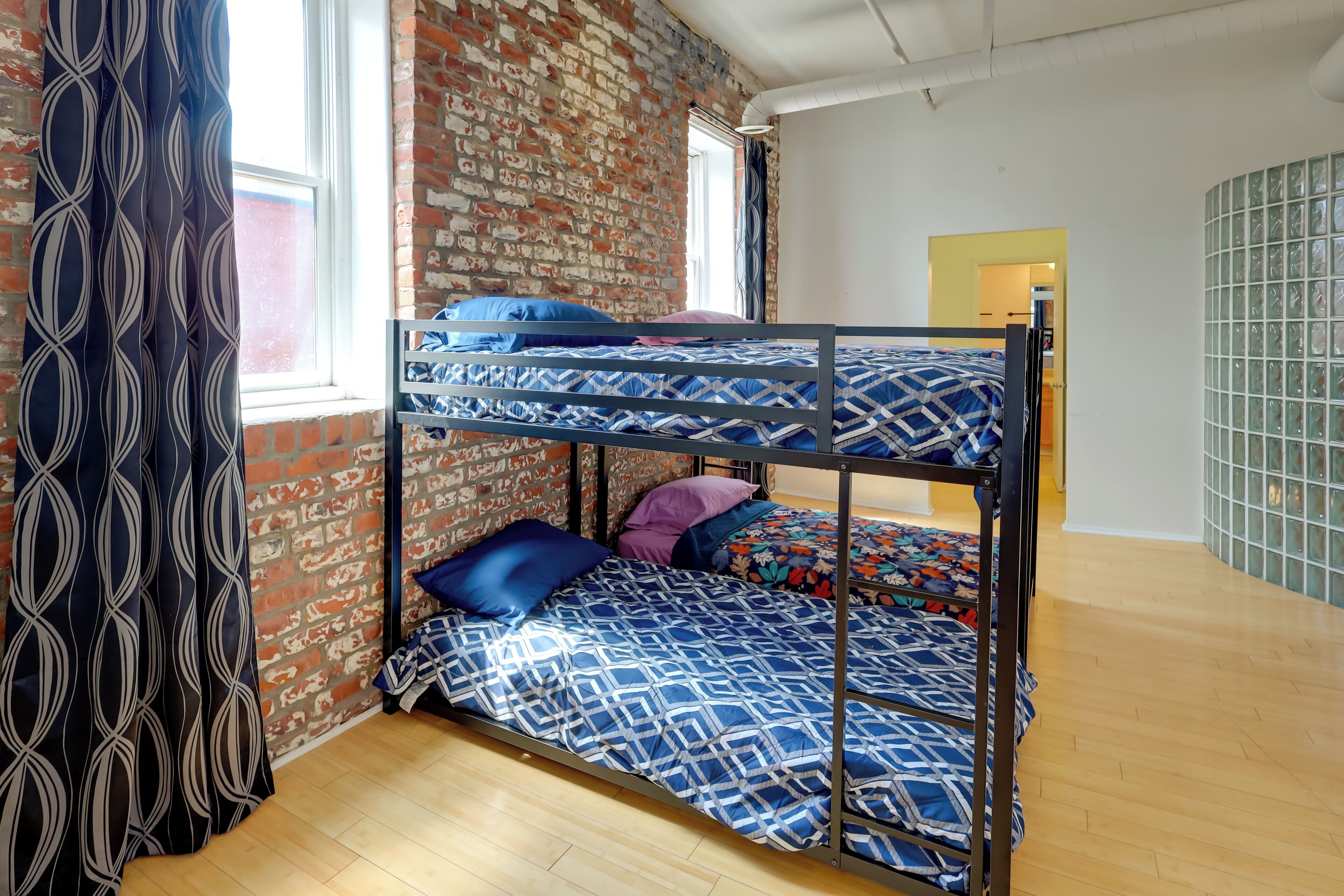 A bunk bed room with patterned bedding, a brick wall, and a window.