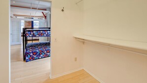 A room with a bunk bed, wooden flooring, and a white wall.