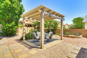 Un patio cubierto con una pérgola, mobiliario exterior y un sendero de grava.