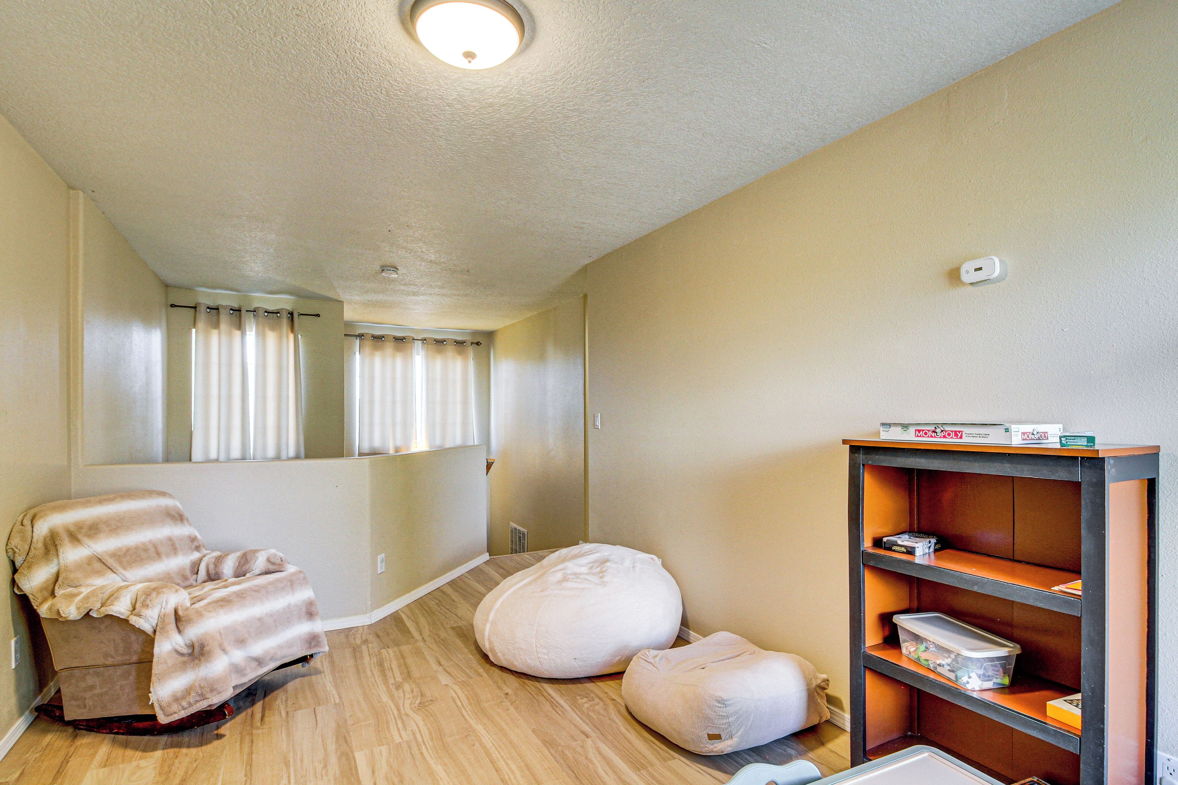 A room with a wooden floor, a white bean bag chair, a cushioned chair, a bookshelf with board games, and a ceiling light.