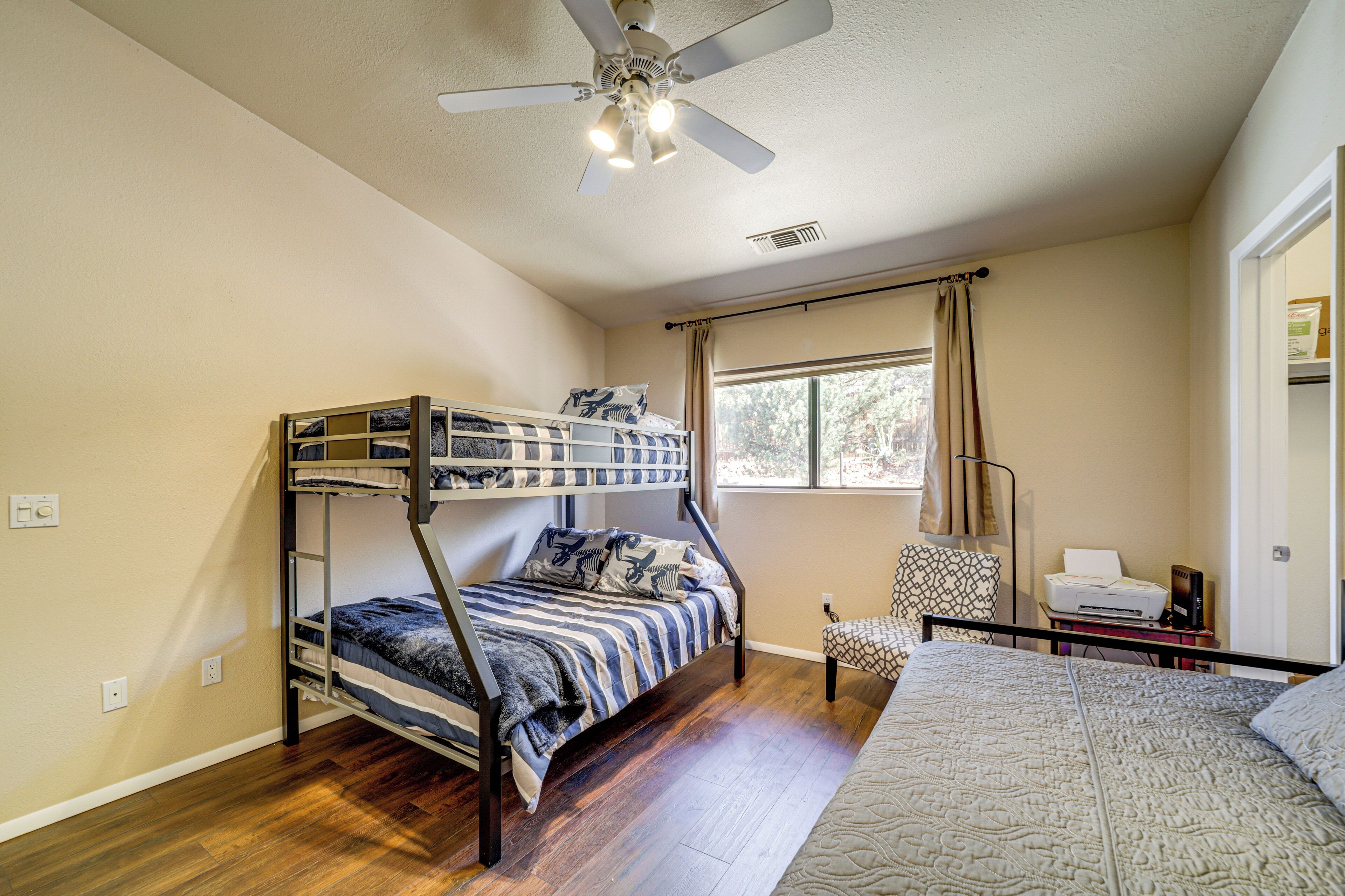 A room with a bunk bed, a desk with a printer, a chair, and a window with curtains.