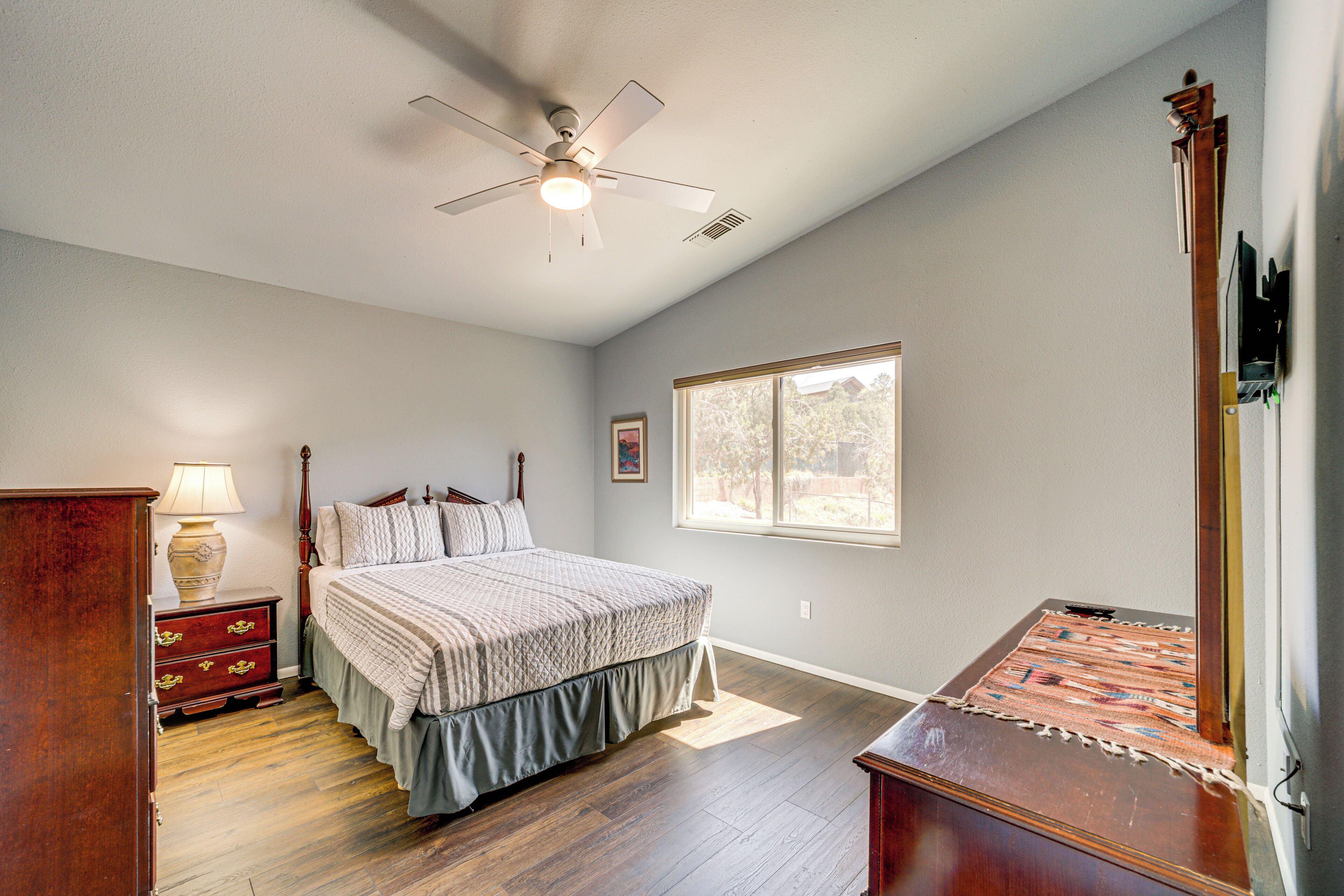 A bedroom with a bed, wooden nightstand, lamp, and a ceiling fan.