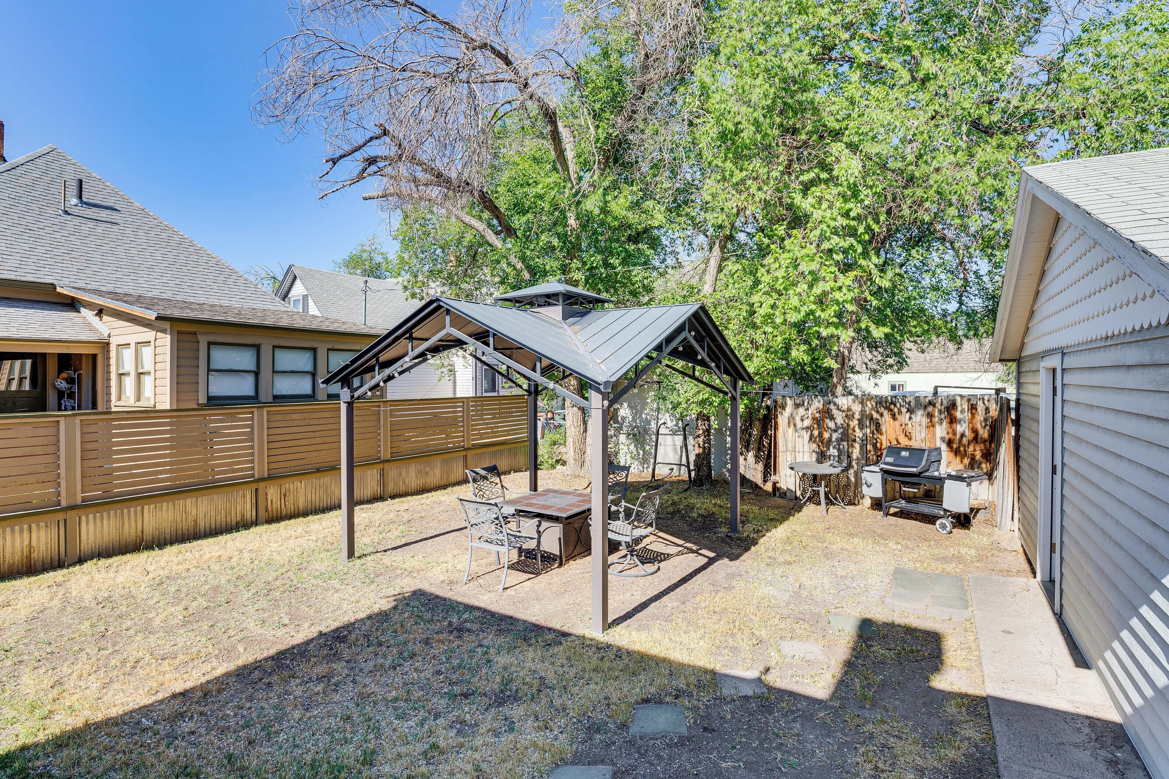 A backyard with a covered patio, a grill, and a wooden fence.