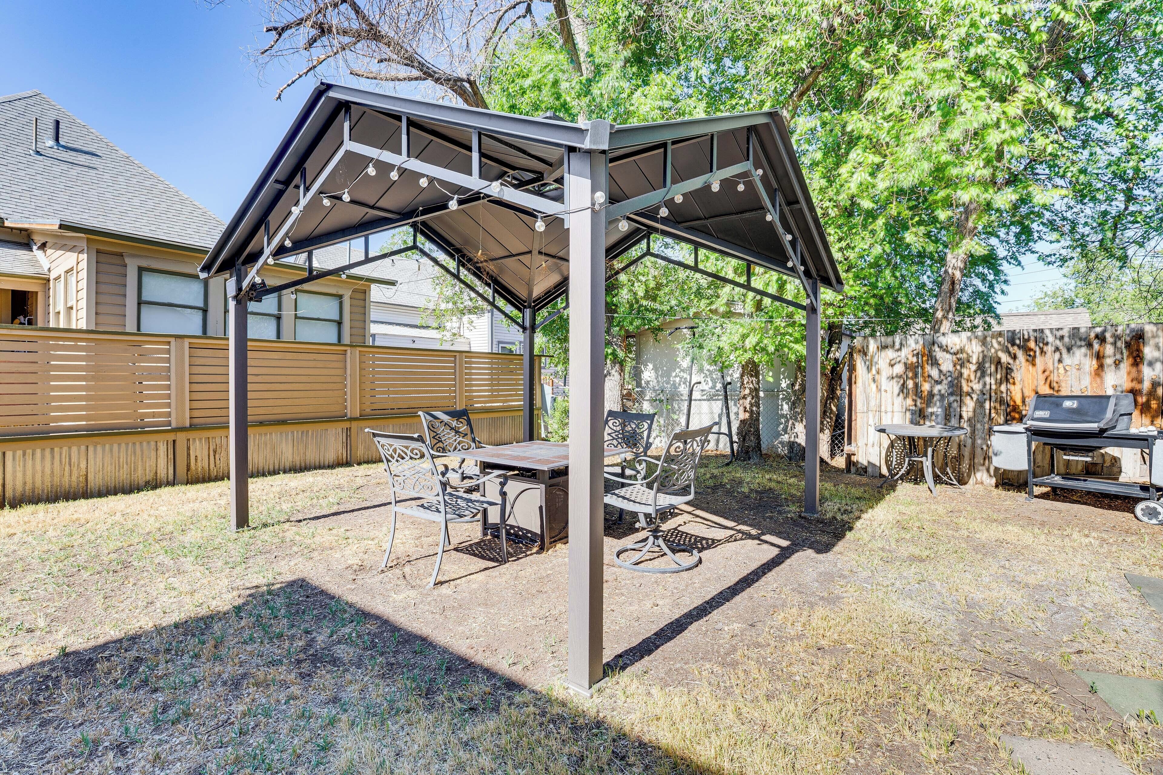 A covered patio area with a table and chairs, a grill, and a wooden fence in the background.