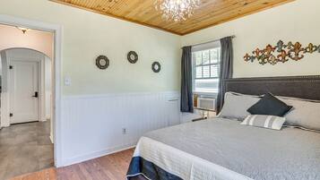Ein Schlafzimmer mit Holzbalkendecke, einem Bett mit grau-weißer Tagesdecke und drei dekorativen Wandspiegeln.