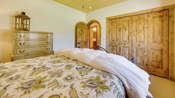 Une chambre à coucher comprenant un lit, une commode, une porte en arc de cercle et une armoire en bois.