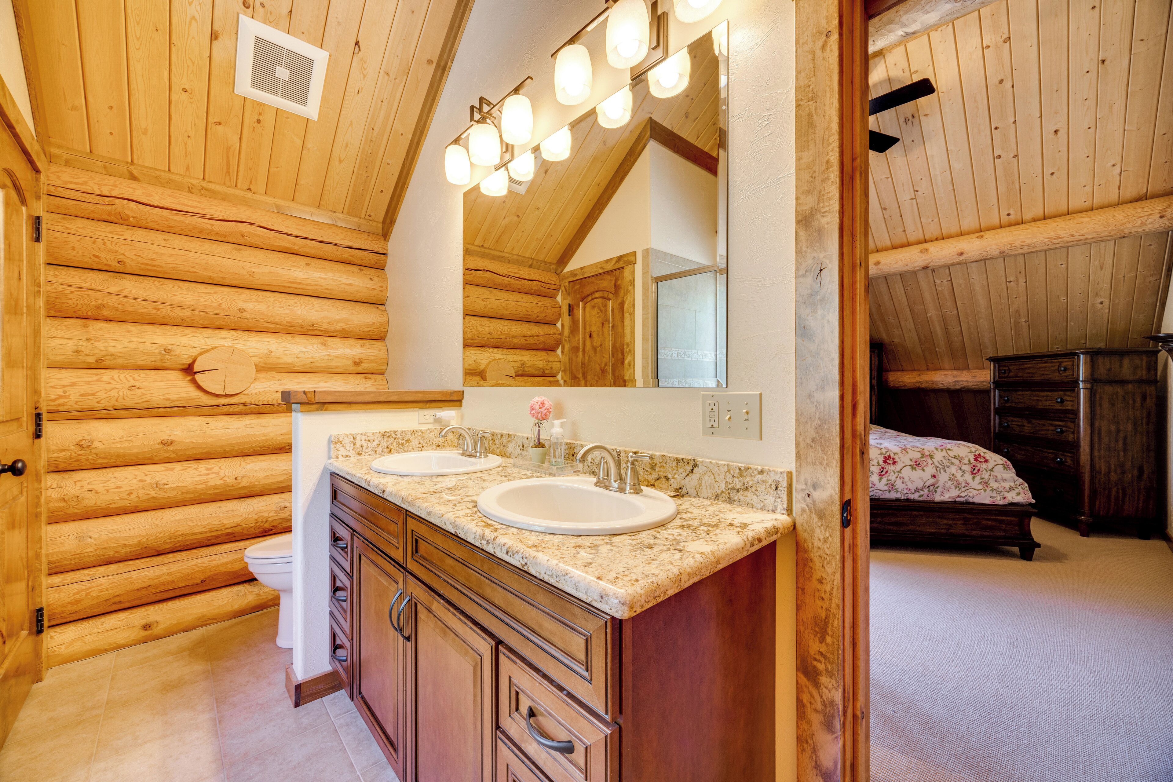 Une salle de bain rustique, aménagée dans une cabane en rondins, avec deux lavabos, un miroir et un plafond en bois.