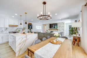 A modern kitchen with white cabinets, a marble island, and a wooden dining table. - Walk to The Village Shops/eats: Big Bear Lake Home (Big Bear Lake)