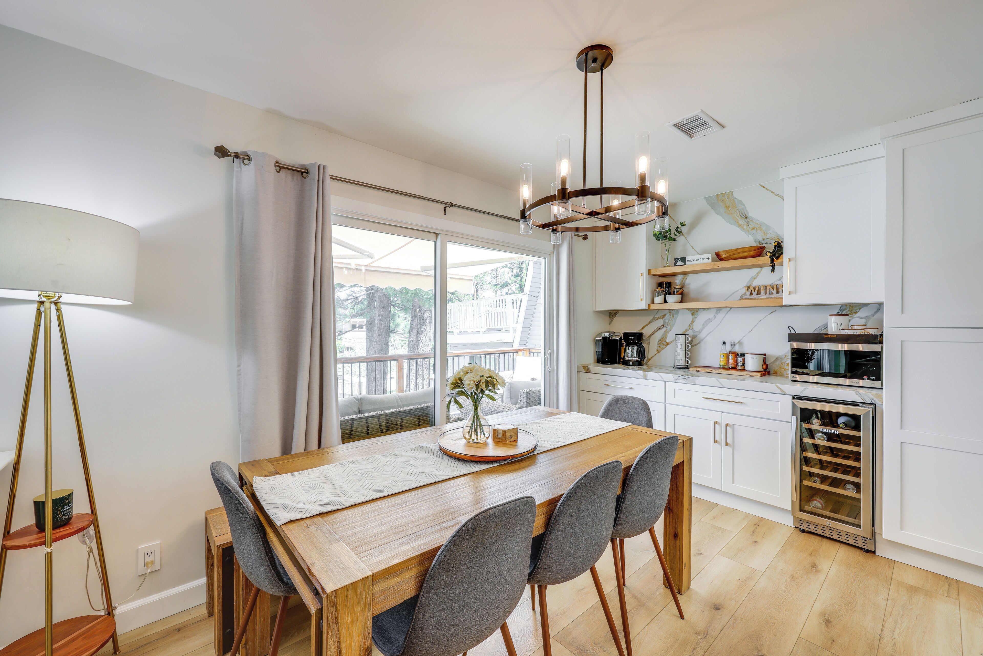 A modern kitchen with white cabinets, a wooden dining table, and a chandelier.
