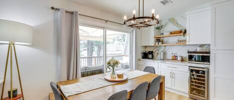 A modern kitchen with white cabinets, a wooden dining table, and a chandelier.