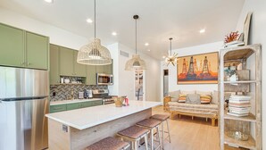 Een moderne keuken met een centraal eiland, groene kasten, roestvrijstalen apparatuur en een zithoek met een bank en barstoelen.