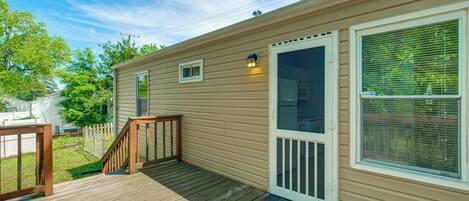 A single-story mobile home with a wooden deck, a front door with a glass panel, and a small window.