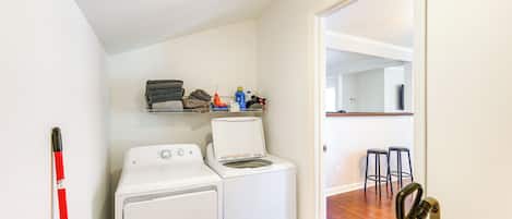A laundry area with two washing machines, a drying rack, and a vacuum cleaner.