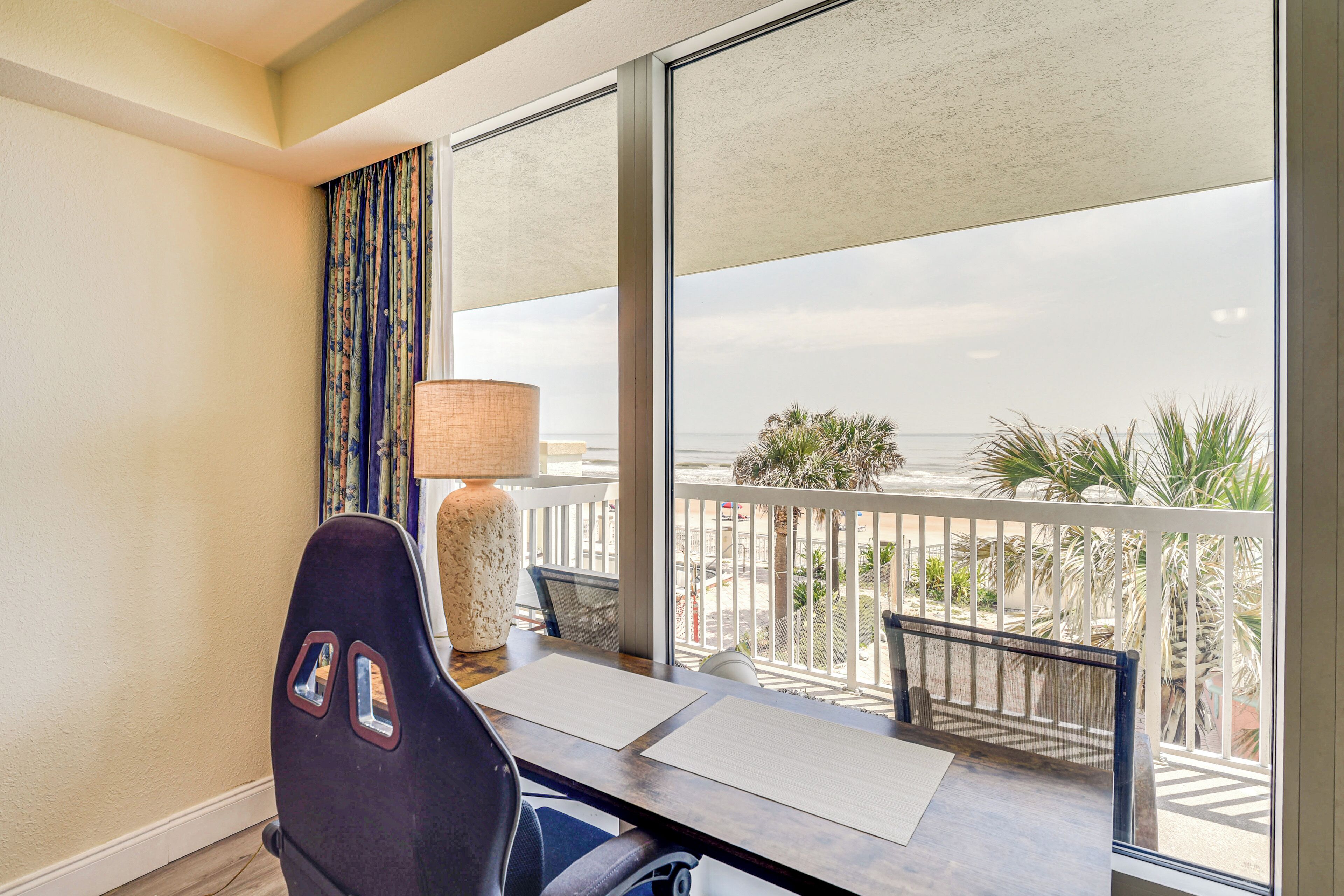 Une chambre d’hôtel avec un balcon, un bureau, une chaise, une lampe et une vue sur l’océan.