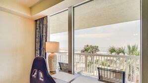Een hotelkamer met balkon, bureau, stoel, lamp en uitzicht op de oceaan.