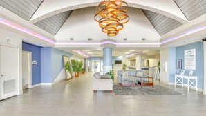 Een ruime lobby met een modern plafondontwerp, een receptiebalie en een zithoek met een bijzettafeltje.