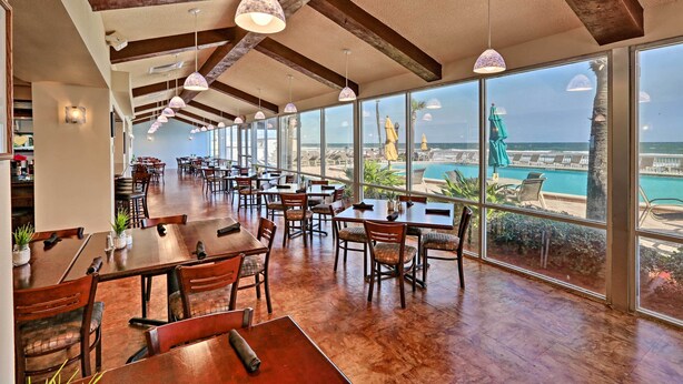 Een ruime eetruimte met houten tafels en stoelen, grote ramen met uitzicht op de zee en een zwembad.