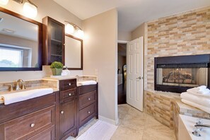 Une salle de bain avec un grand miroir, deux lavabos, un meuble-lavabo en bois foncé, une serviette blanche et une cheminée.