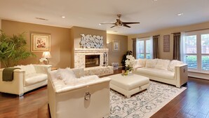 A spacious living room with a fireplace, white furniture, and a large window with curtains. - Large Luxury Home With Saltwater Pool (Denton)