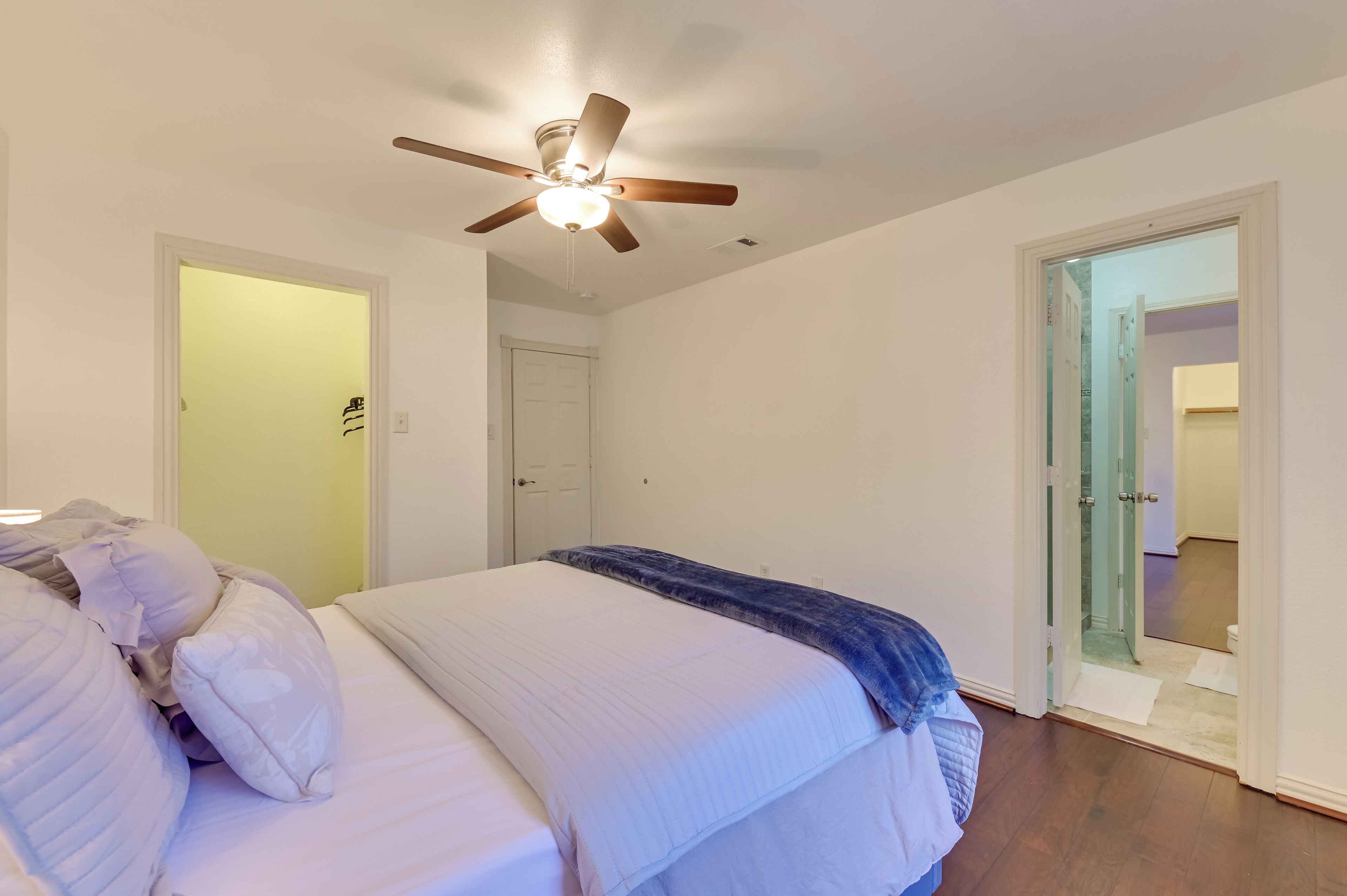 A bedroom with a bed, a ceiling fan, and a door leading to another room.