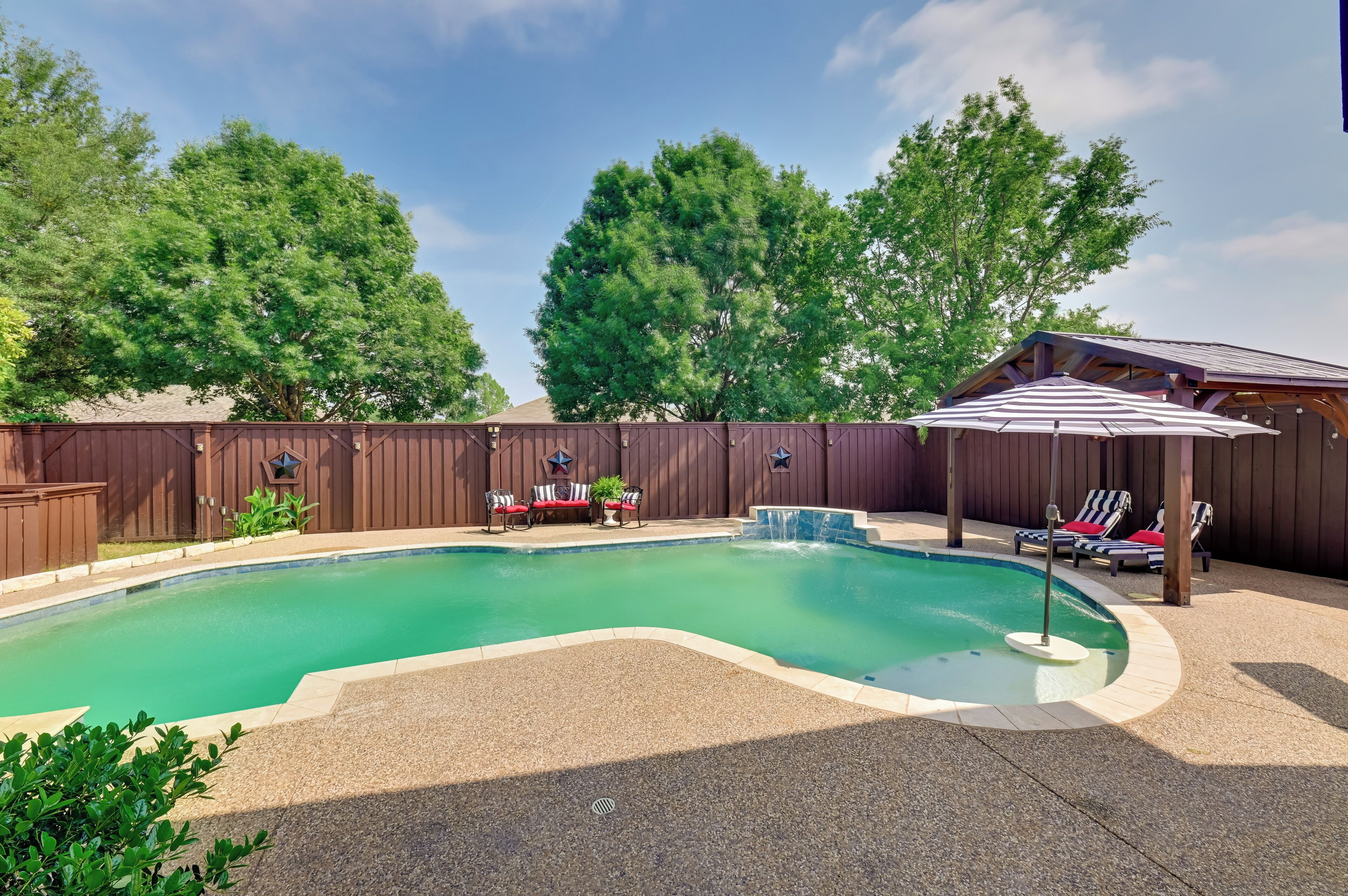 A backyard with a swimming pool, lounge chairs, and a covered patio area.
