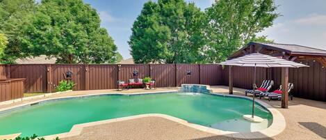 A backyard with a swimming pool, lounge chairs, and a covered patio area.