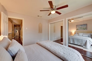 Relax in this serene bedroom with a large bed, mirror, and nightstand, complete with a ceiling fan and door to a separate room.