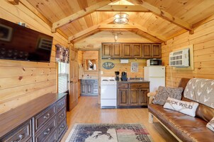 Interior acogedor de una cabaña con paredes de madera, una zona de cocina, un sofá de cuero y un televisor de pantalla plana.