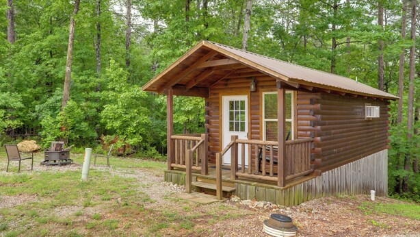 A small log cabin with a porch, surrounded by trees. - 1 Mi to Current River: Cozy Studio Cabin! (Van Buren)