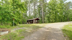 A rustic cabin with a gravel driveway leading to it, surrounded by dense forest. - 1 Mi to Current River: Cozy Studio Cabin! (Van Buren)