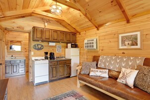 Interior de una cabaña de madera con cocina, comedor y sala de estar con sofá de cuero.