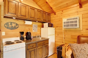 Una cocina de cabaña de madera con estufa, pileta, refrigerador y microondas.