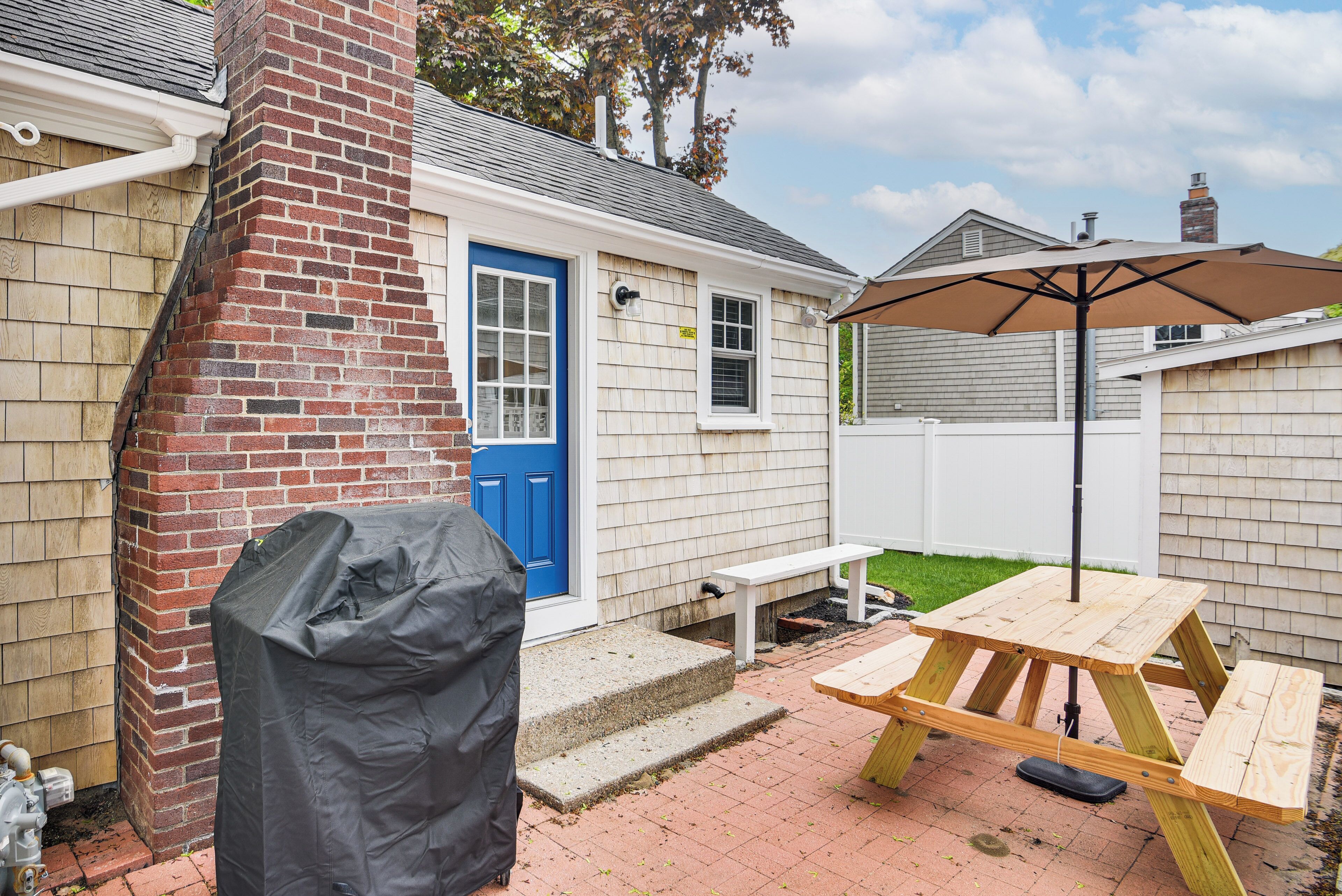 Ein Garten mit Grill, Picknicktisch und Sonnenschirm.