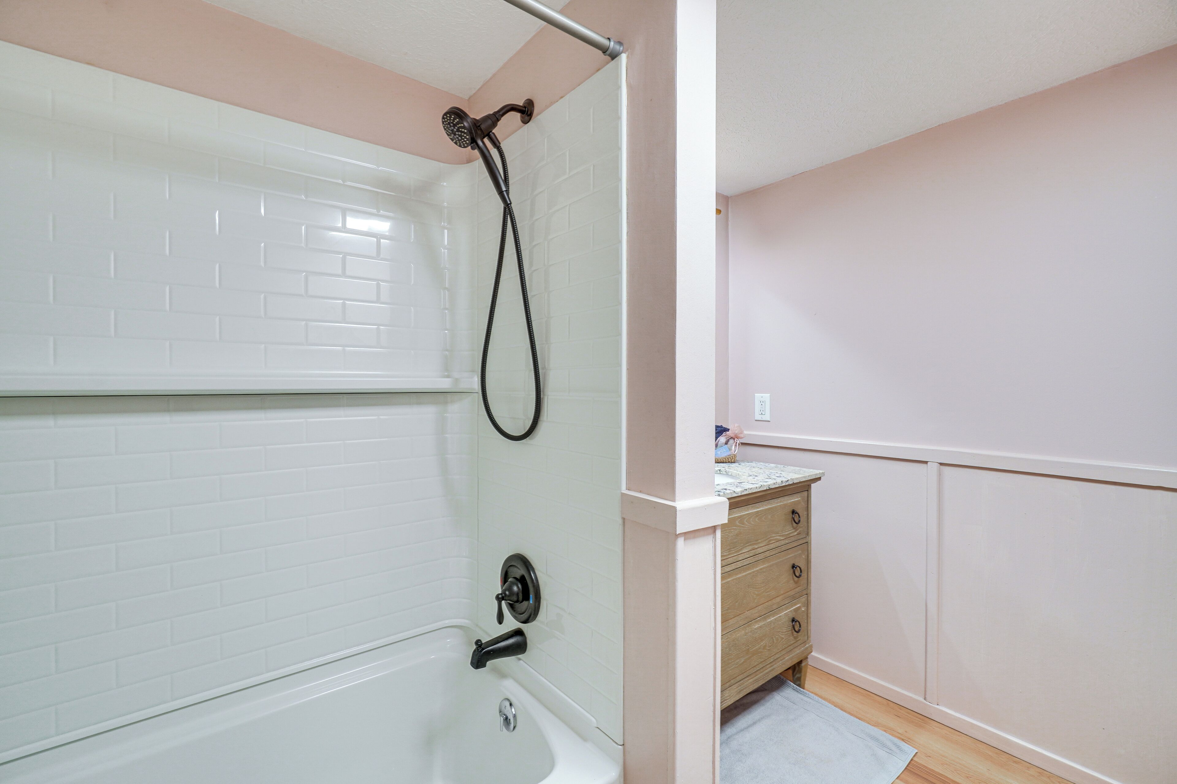 Un baño con una bañera blanca, un cabezal de ducha y un mueble de madera con cajones.