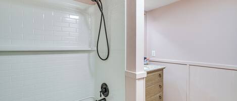 Un baño con una bañera blanca, un cabezal de ducha y un mueble de madera con cajones.