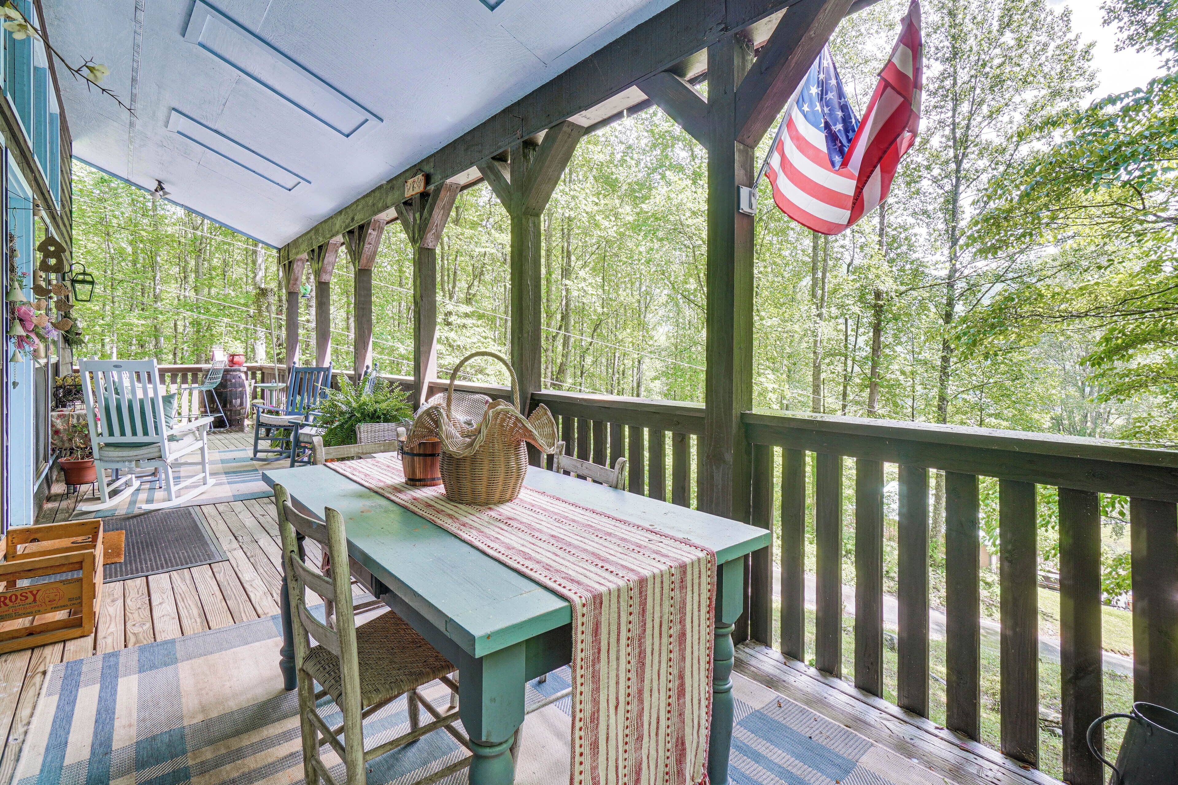 A wooden deck with a table and chairs, an American flag, and a view of a forest. - 4 Mi to Lake Santeetlah: Cabin w/ Deck & Views (Robbinsville)